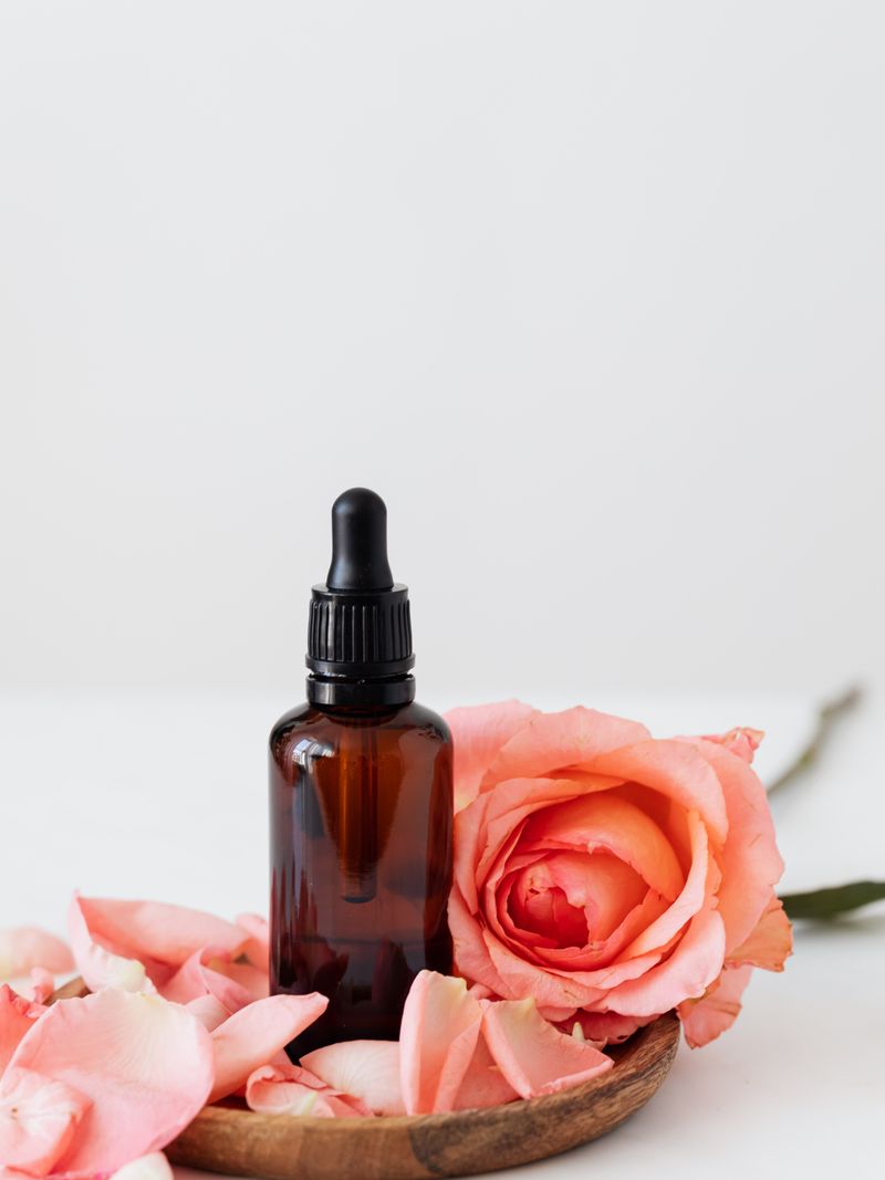 Aurore Radiance Serum — amber glass dropper bottle beside a fresh pink rose on clean white surface