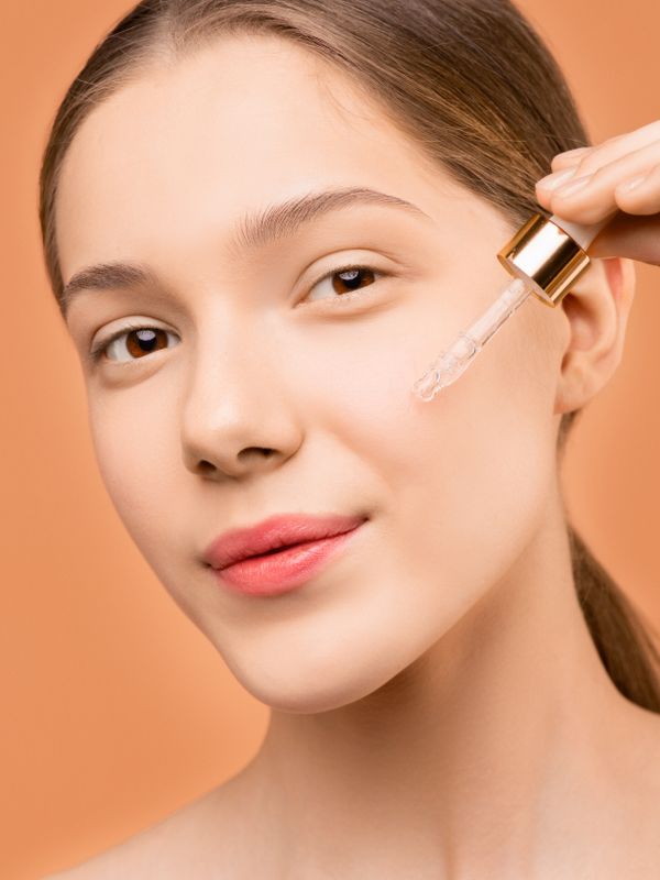 Step 2 Treat — person applying serum with glass dropper to face, warm natural light, serene skincare ritual close-up