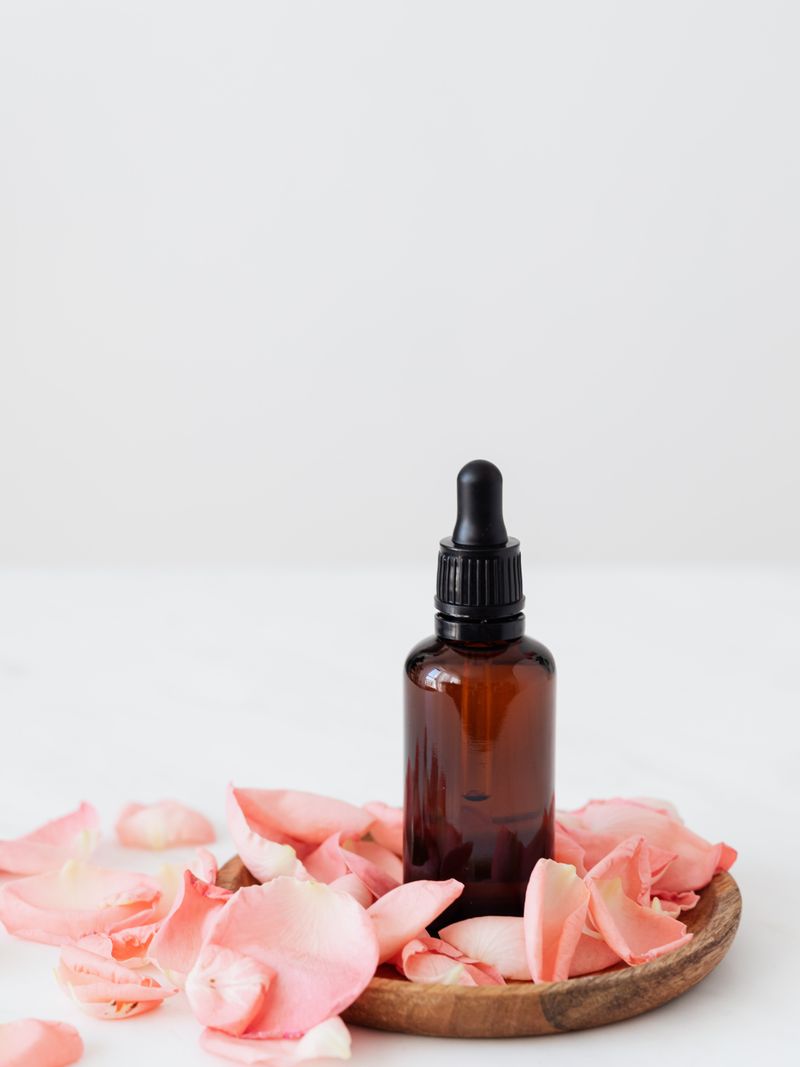 Solstice Facial Oil — amber glass dropper bottle surrounded by dense rose petals, warm botanical editorial styling