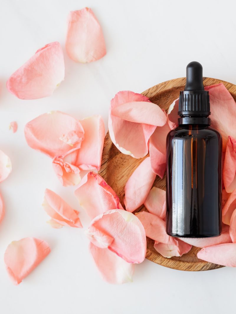 Veil Barrier Cream — amber dropper bottle surrounded by scattered rose petals on warm natural wood surface